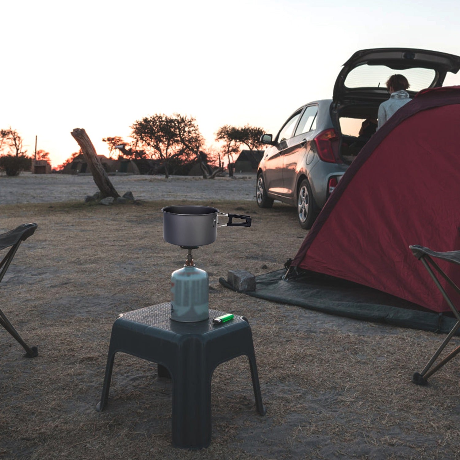 Camping setup with a portable stove and pot near a tent and car at sunset.